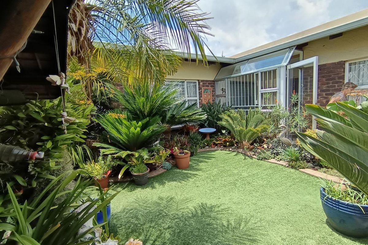 A private rear courtyard featuring artificial turf, established garden beds, and direct access to the home through glass doors with security bars.