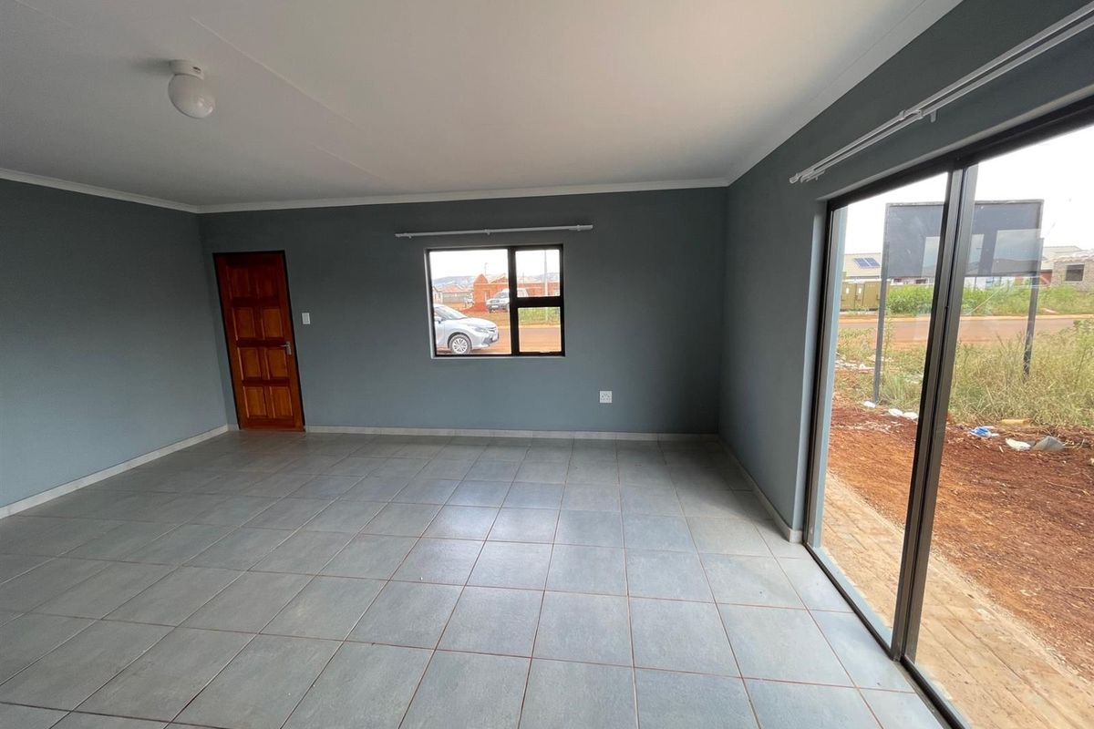A bright, empty living room featuring neutral grey walls, tiled flooring, and a large sliding glass door providing access to the exterior.