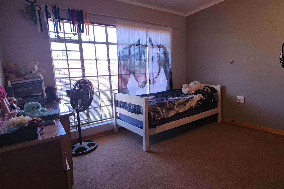A bedroom featuring carpeted flooring, a large window with security bars, and neutral wall finishes.