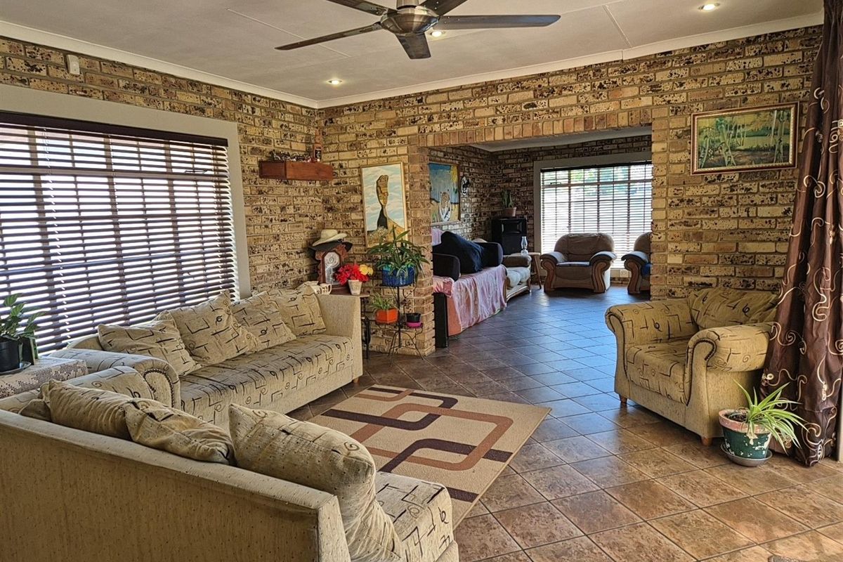 Spacious living area featuring exposed face-brick walls, tiled flooring, and a ceiling fan, offering a rustic and open-plan layout.