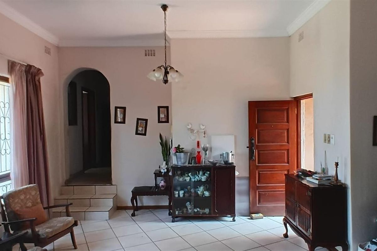 A living area featuring tiled flooring, an arched doorway leading to a raised hallway, and a traditional wooden door.