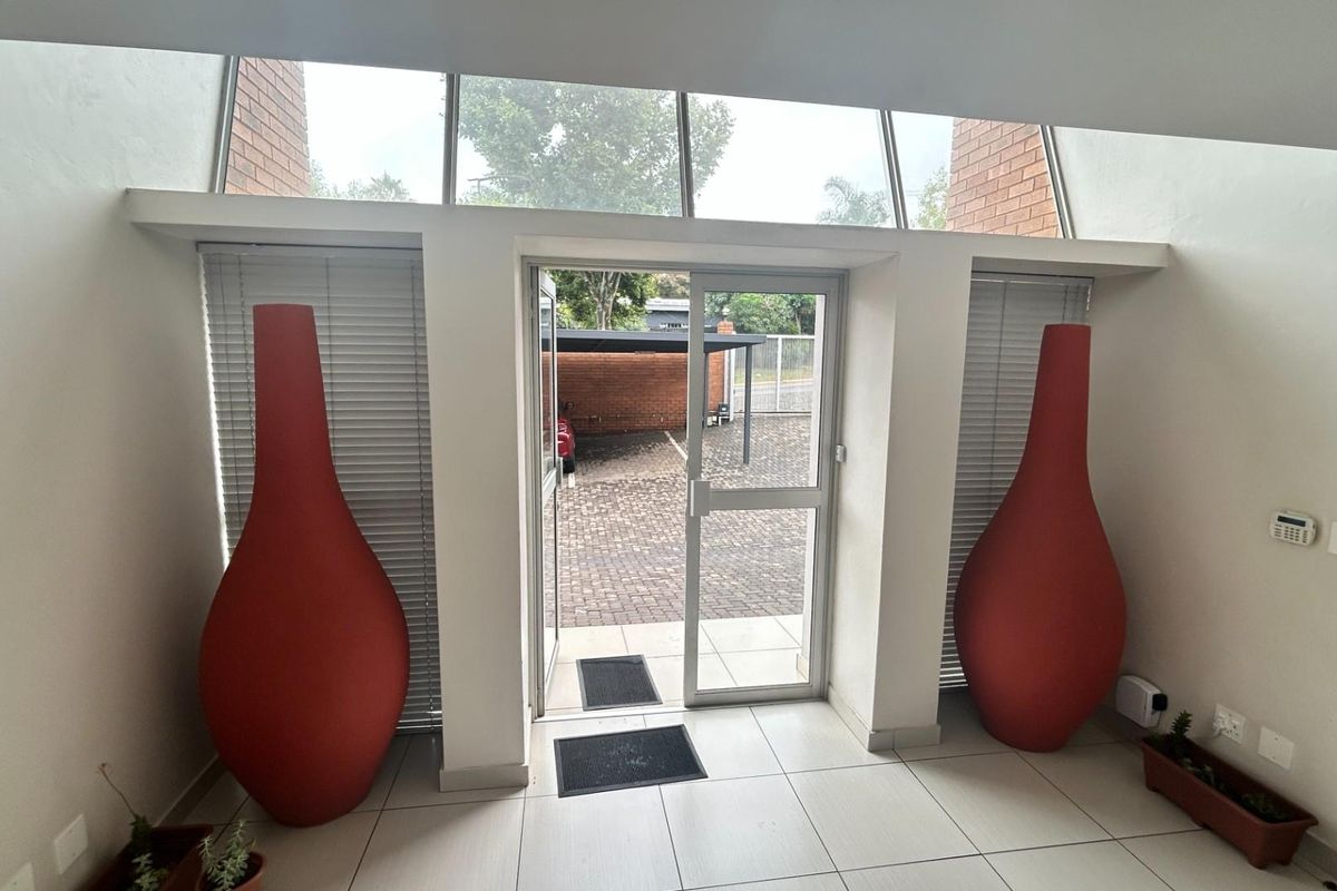 Bright office entrance featuring large glass panels, tiled flooring, and a secure glass door leading to an exterior paved parking area.
