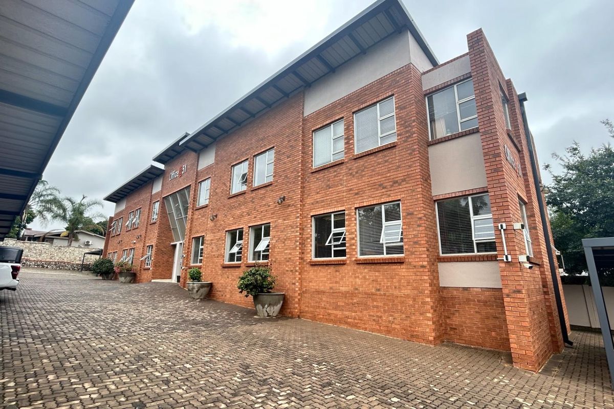 A multi-story office building featuring a classic red brick facade, paved driveway, and covered parking bays.