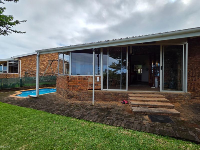 Rear view of the townhouse featuring a covered patio, brick facade, sliding glass doors, and an adjacent swimming pool set in a garden.