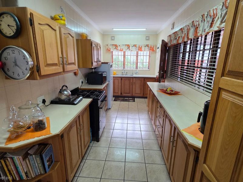 A functional galley-style kitchen featuring traditional timber cabinetry, tiled flooring, and ample counter space with a built-in stove and double sink.