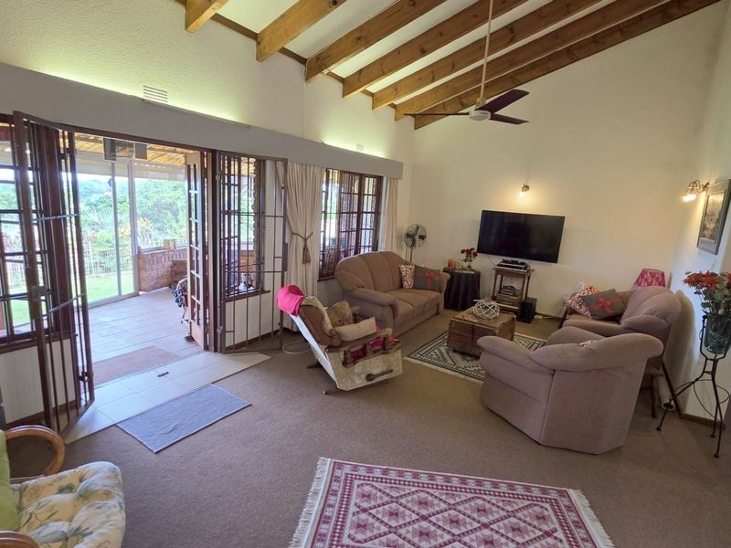Spacious living room featuring vaulted ceilings with exposed timber beams, ceiling fan, and large glass doors opening onto a covered patio area.