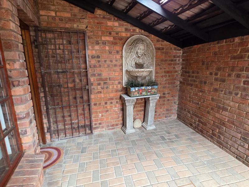 A covered patio area featuring exposed brick walls, paved flooring, and a decorative wall-mounted fountain feature.