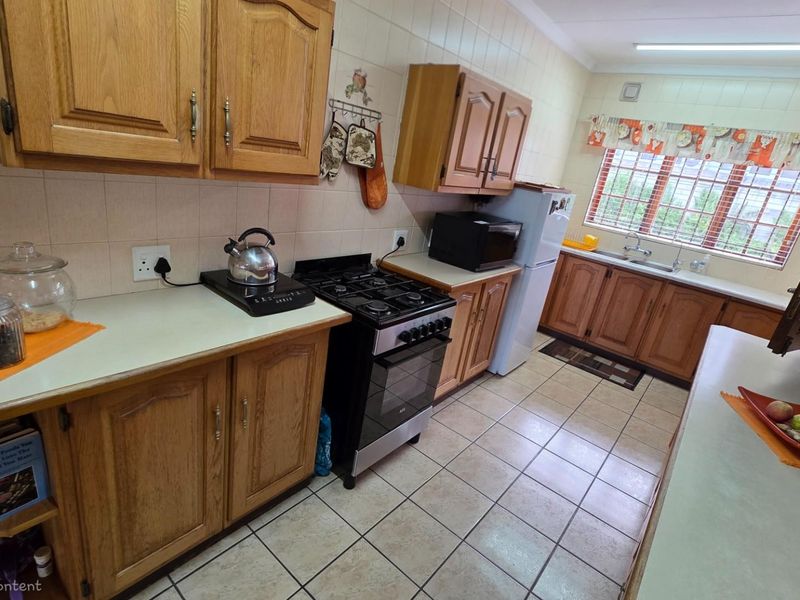 A functional kitchen featuring traditional wooden cabinetry, tiled splashbacks, a gas stove, and a double basin sink with a window view.