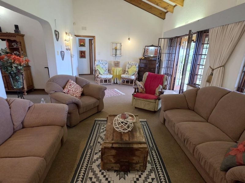 Spacious living room featuring high vaulted ceilings with exposed timber beams, carpeted flooring, and large glass doors providing access to the outdoor area.