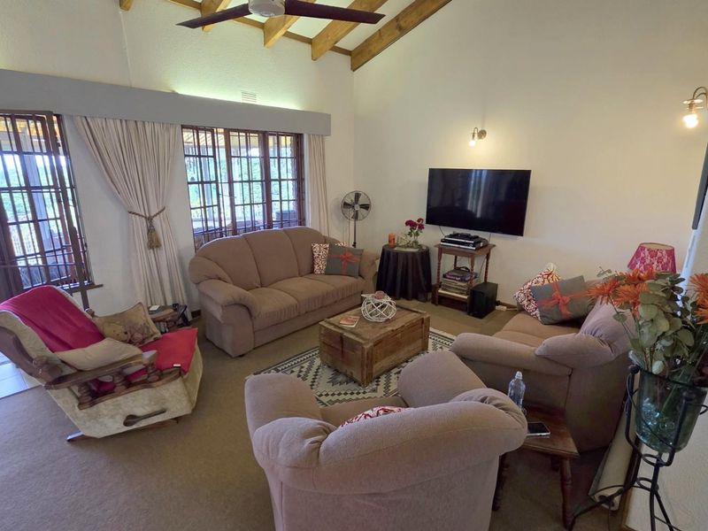 Spacious living room featuring high vaulted ceilings with exposed timber beams, large windows, and sliding glass doors leading to an outdoor patio area.