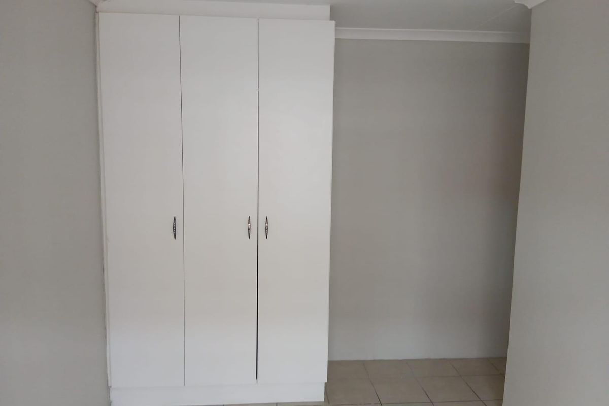 A clean, empty bedroom featuring a white built-in wardrobe and neutral tiled flooring, providing a blank canvas for personalization.