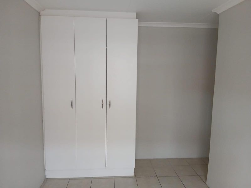A clean, empty bedroom featuring a white built-in wardrobe and neutral tiled flooring, providing a blank canvas for personalization.