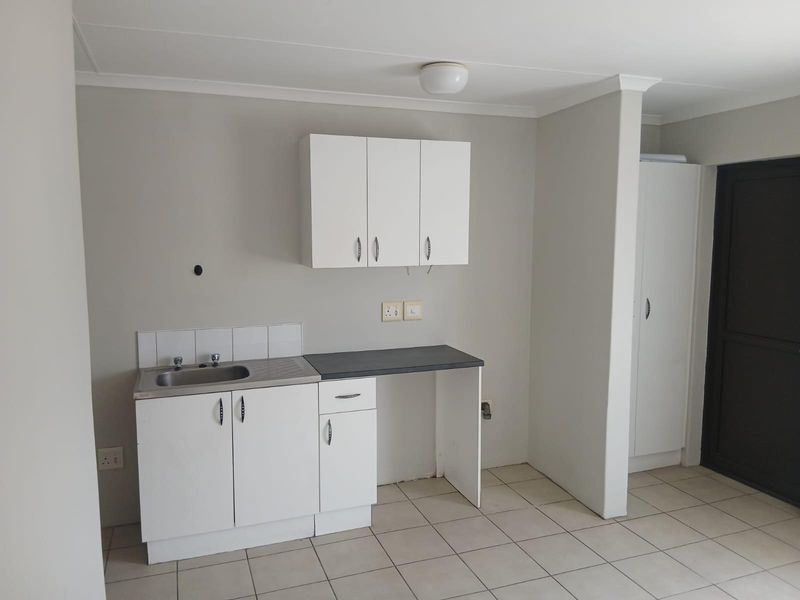 A compact kitchen area featuring white built-in cabinetry, a stainless steel sink, and tiled flooring, providing a functional and clean utility space.