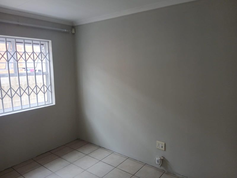 A clean, empty bedroom featuring neutral walls, tiled flooring, and a window fitted with a security gate.