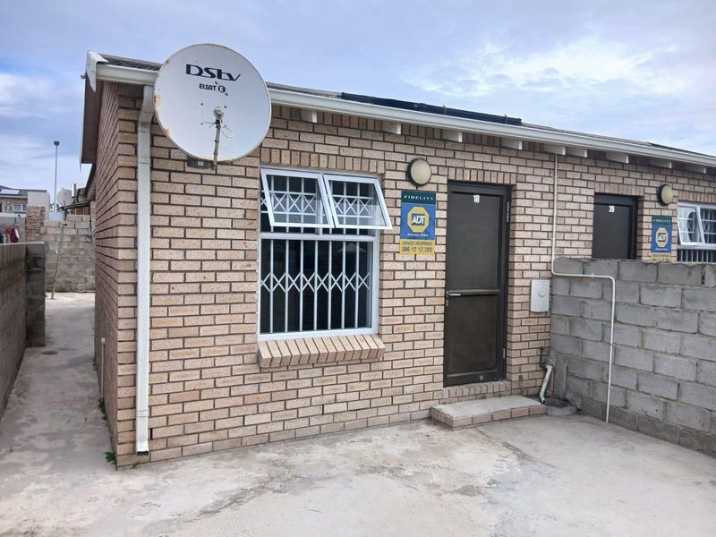 Exterior view of a face brick residential unit featuring security bars on windows and a concrete paved area.