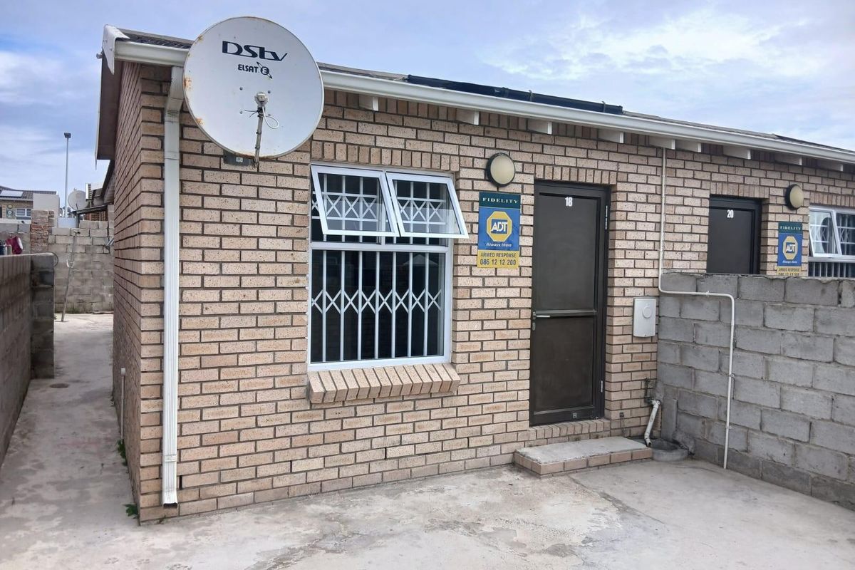 Exterior view of a face brick residential unit featuring security bars on windows and a concrete paved area.