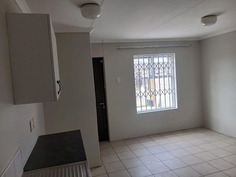 A clean, empty kitchen area featuring tiled flooring, built-in cabinetry, and a window fitted with a security gate.