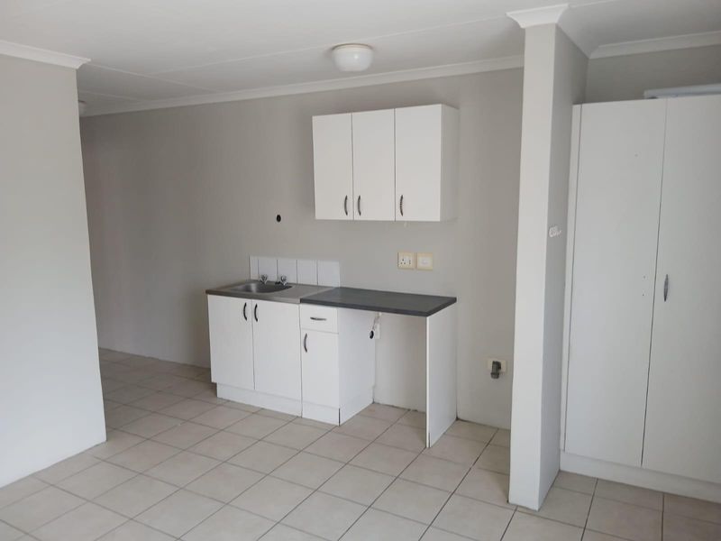 A compact, functional kitchen area featuring white cabinetry, a stainless steel sink, laminate countertops, and neutral tiled flooring in an open-plan layout.