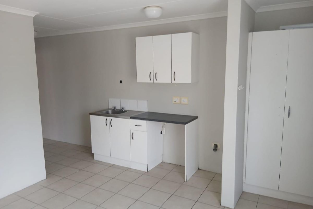 A compact, functional kitchen area featuring white cabinetry, a stainless steel sink, laminate countertops, and neutral tiled flooring in an open-plan layout.