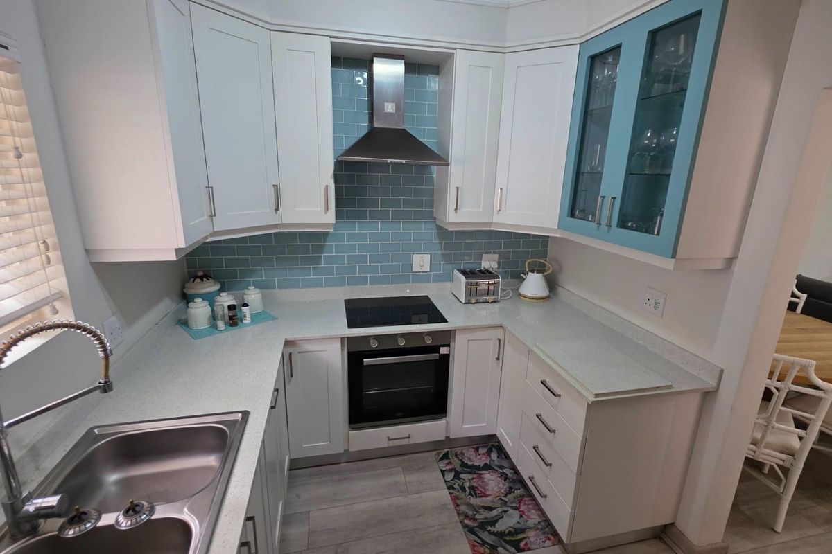 A well-maintained kitchen featuring white cabinetry, a blue subway tile backsplash, stone countertops, a built-in oven, and a stainless steel extractor fan.