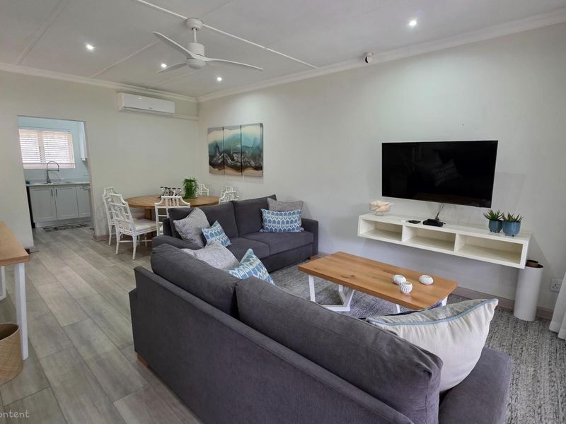 Open-plan living and dining area featuring light wood-look flooring, recessed ceiling lighting, a ceiling fan, and a wall-mounted air conditioning unit.