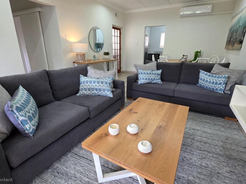 A bright and open-plan living area featuring a wall-mounted air conditioning unit, neutral finishes, and seamless flow into the adjacent dining and kitchen spaces.