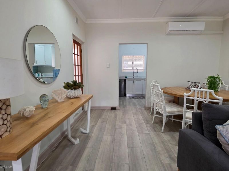 Open plan living and dining area featuring wood-look flooring, crown molding, and a wall-mounted air conditioning unit, with a view into the adjacent kitchen.
