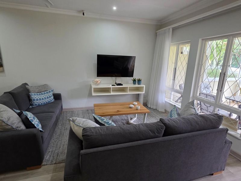 A bright and comfortable living room featuring large windows with security bars, recessed ceiling lighting, and a wall-mounted media console.
