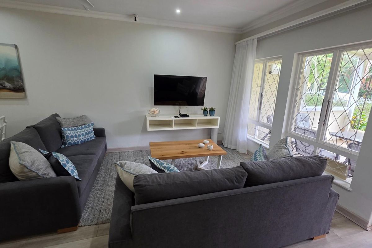 A bright and comfortable living room featuring large windows with security bars, recessed ceiling lighting, and a wall-mounted media console.