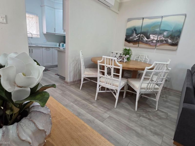 An open-plan living and dining area featuring light wood-look flooring, with a view into the adjacent kitchen space.