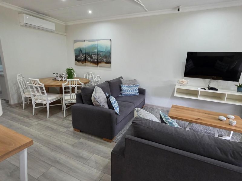 Open-plan living and dining area featuring light wood-look flooring, recessed ceiling lighting, and a wall-mounted air conditioning unit.