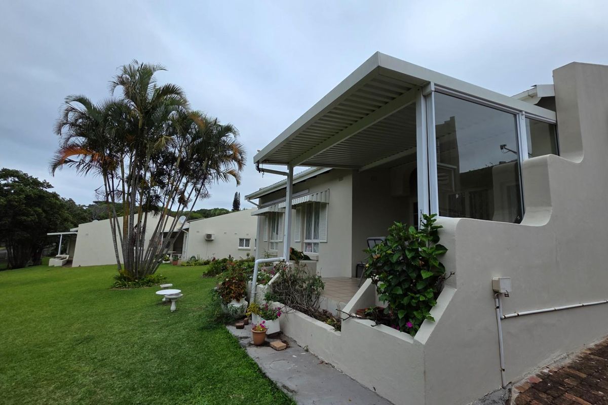 A rear view of the townhouse featuring a covered patio area, concrete flooring, and access to a shared garden space.