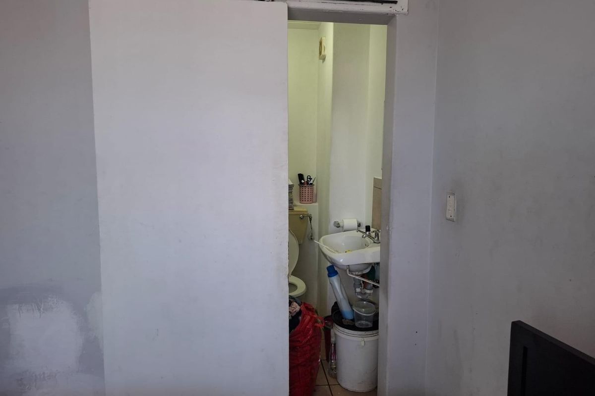 A small, dated bathroom featuring a wall-mounted basin and toilet, accessed via a sliding barn-style door.