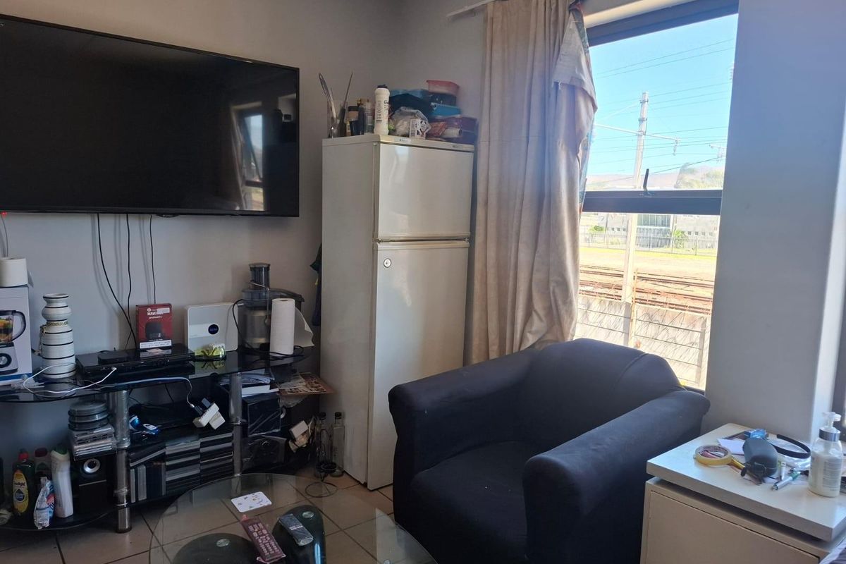 A compact living area featuring tiled flooring and a large window with natural light, suitable for a small apartment layout.