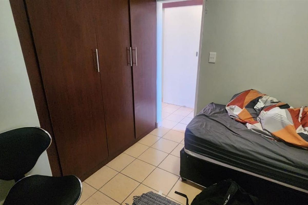 A bedroom featuring built-in wooden cupboards and tiled flooring, with direct access to an adjoining room.