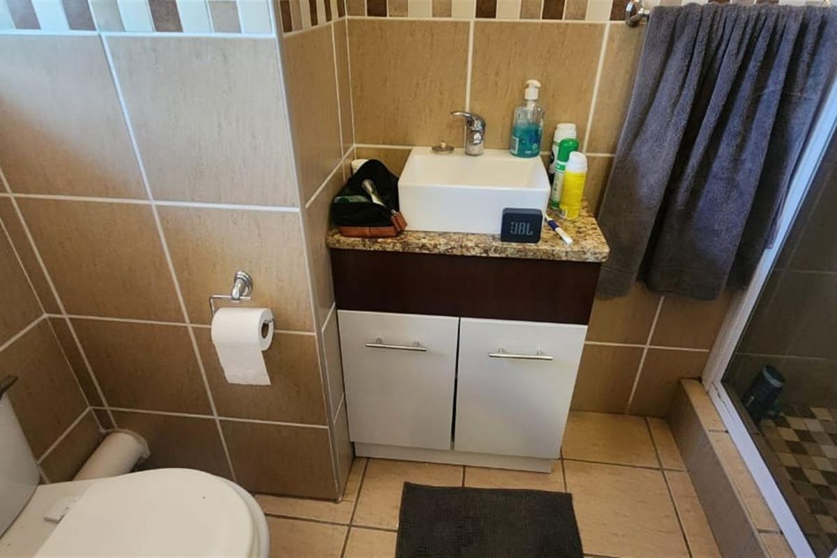 A compact bathroom featuring a vanity with a vessel sink, a toilet, and a tiled shower enclosure with neutral wall and floor tiles.