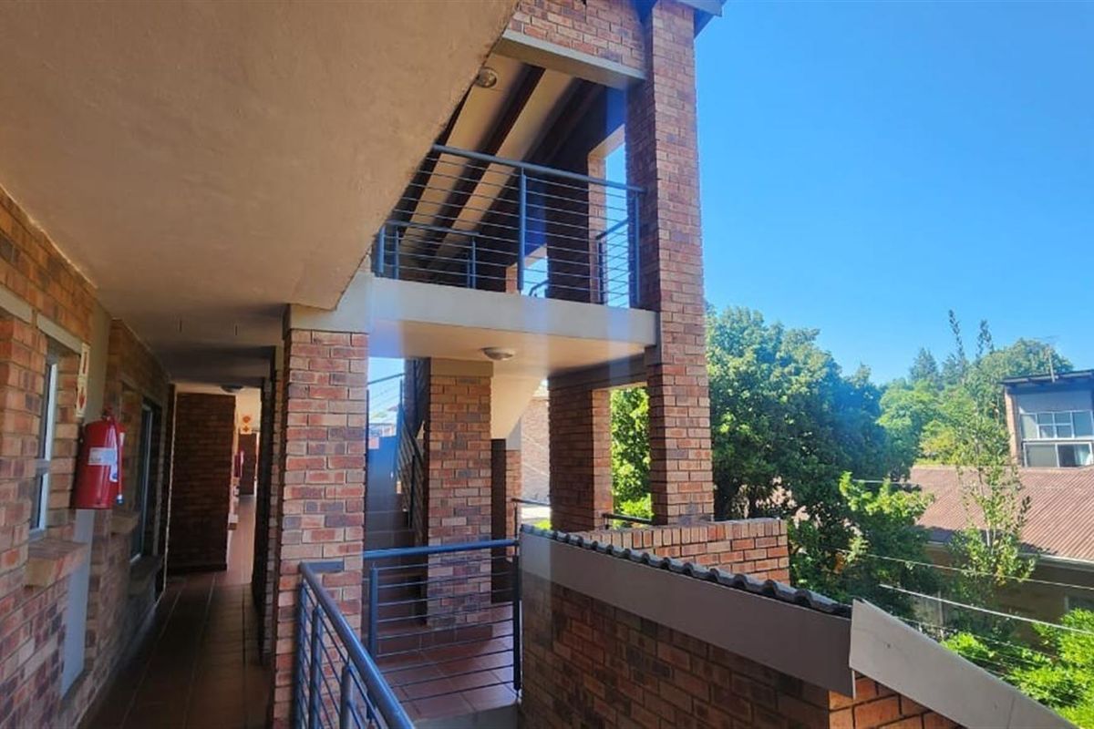 An exterior view of an apartment building walkway featuring exposed brick construction, metal railings, and an open-air staircase design.