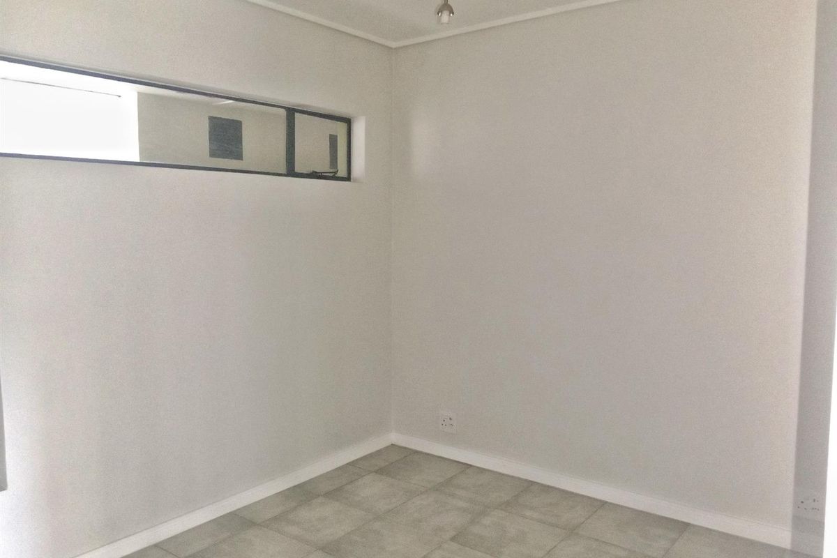 A clean, empty bedroom featuring neutral tiled flooring, crisp white walls, and a high-level window providing natural light.