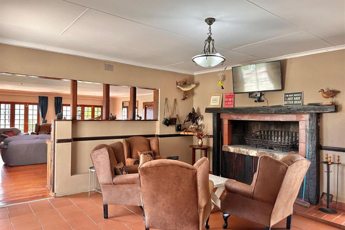 A cozy living room featuring a traditional brick fireplace with a wooden mantel, terracotta floor tiles, and an open-plan layout connecting to adjacent spaces.