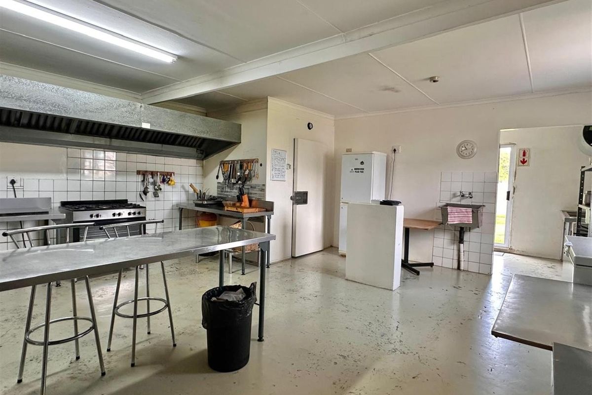 A functional commercial-style kitchen featuring stainless steel prep tables, a large extractor hood, gas stove, and a wall-mounted utility sink.