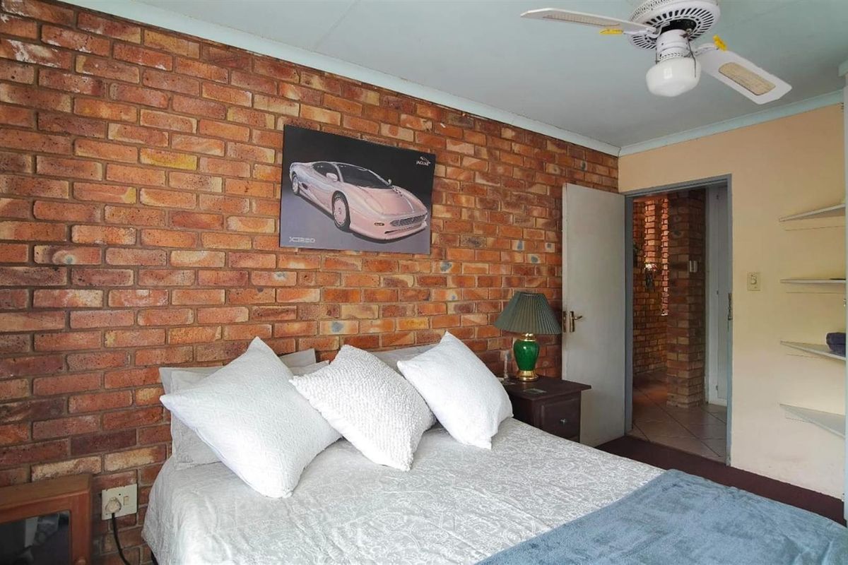 A bedroom featuring a rustic exposed brick feature wall, ceiling fan, and built-in shelving, offering a cozy and character-filled living space.