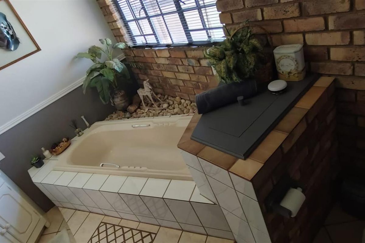 A bathroom featuring a built-in bathtub with tiled surround, exposed brick wall accents, and a vanity basin.