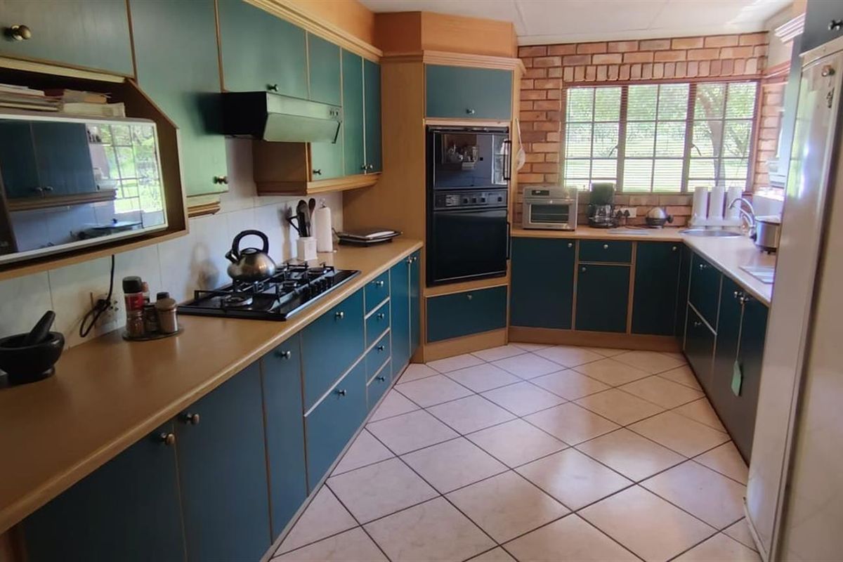 A functional kitchen featuring dark green cabinetry, built-in oven, gas hob, extractor fan, and tiled flooring with a brick feature wall.