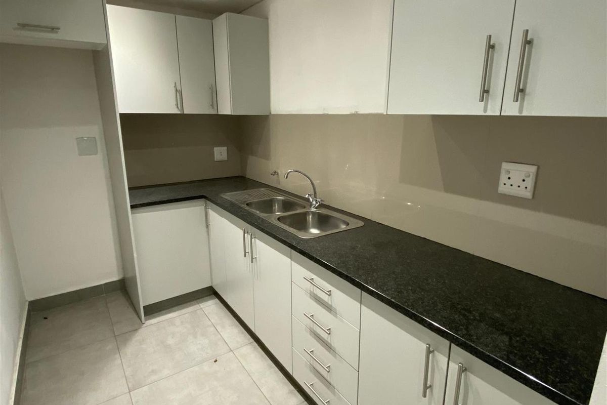 A compact kitchen featuring white cabinetry, dark granite countertops, a double stainless steel sink, and tiled flooring.
