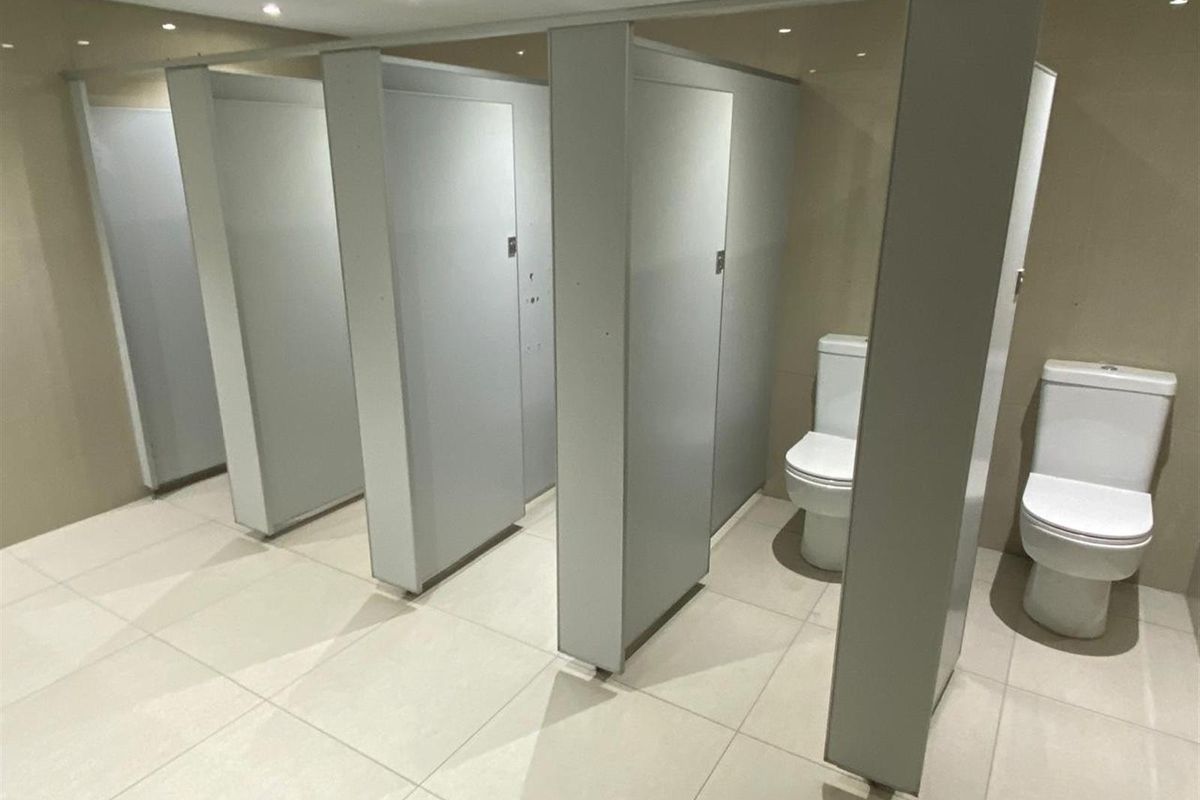 Commercial restroom facility featuring multiple partitioned toilet cubicles with modern white ceramic toilets and neutral floor tiling.