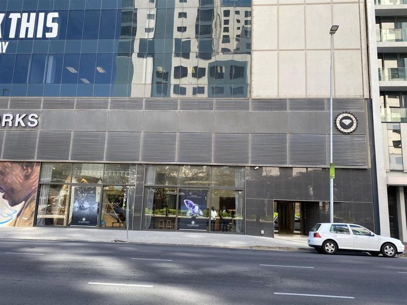 Street-level view of a modern commercial building facade featuring large glass display windows, metal cladding, and prominent signage.