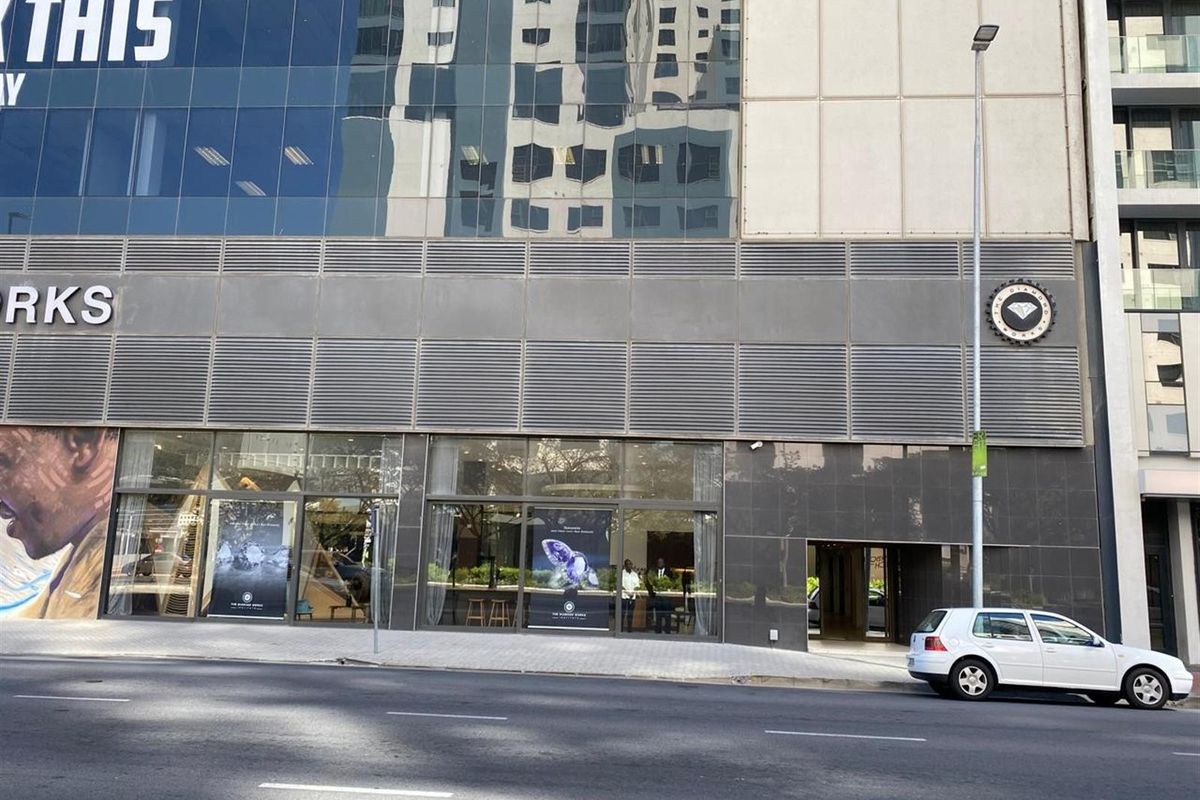Street-level view of a modern commercial building facade featuring large glass display windows, metal cladding, and prominent signage.