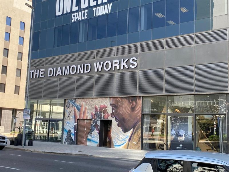 Street-level view of a commercial building facade featuring large glass windows, metal cladding, and a prominent mural at the entrance.