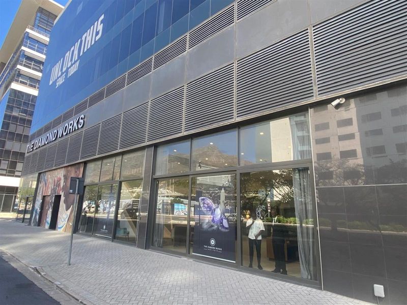Modern commercial building facade featuring extensive glass storefronts, metal louvers, and prominent signage at street level.