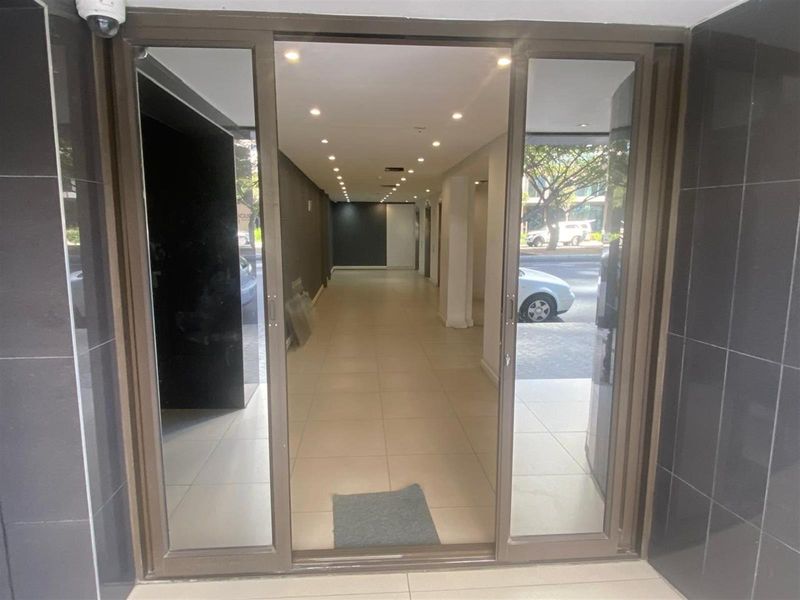 A commercial entrance featuring sliding glass doors, tiled flooring, and recessed downlighting, leading into a clean, open-plan interior space.